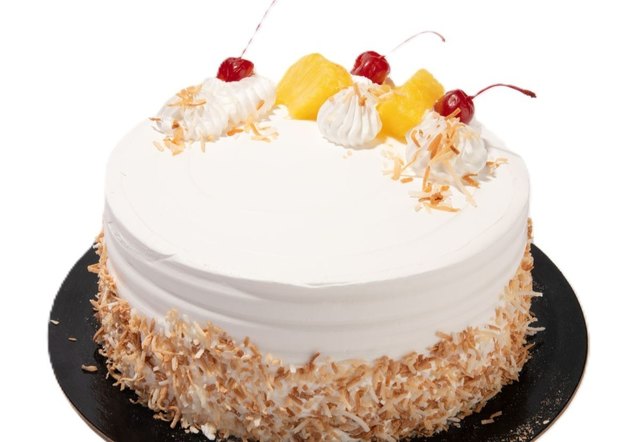 Pina colada cake with white frosting, toasted coconut sides, pineapple chunks, whipped cream, and cherries on top.